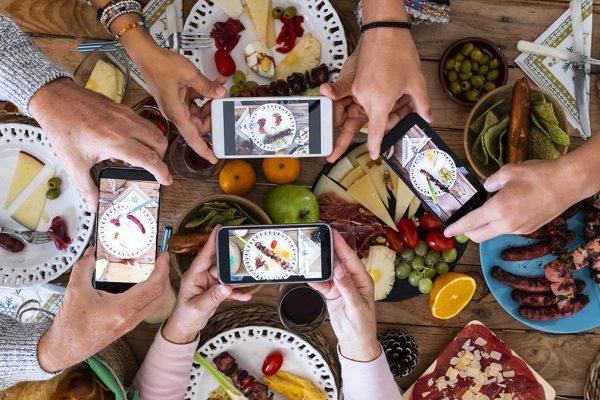 People eating together taking food picture with smartphone to share on social media - concept of celebration - wooden table and mixed food in background