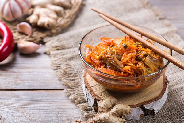 Homemade organic traditional korean kimchi cabbage salad with chopsticks on a wooden table. Fermented vegetarian, vegan preserved gut health food concept